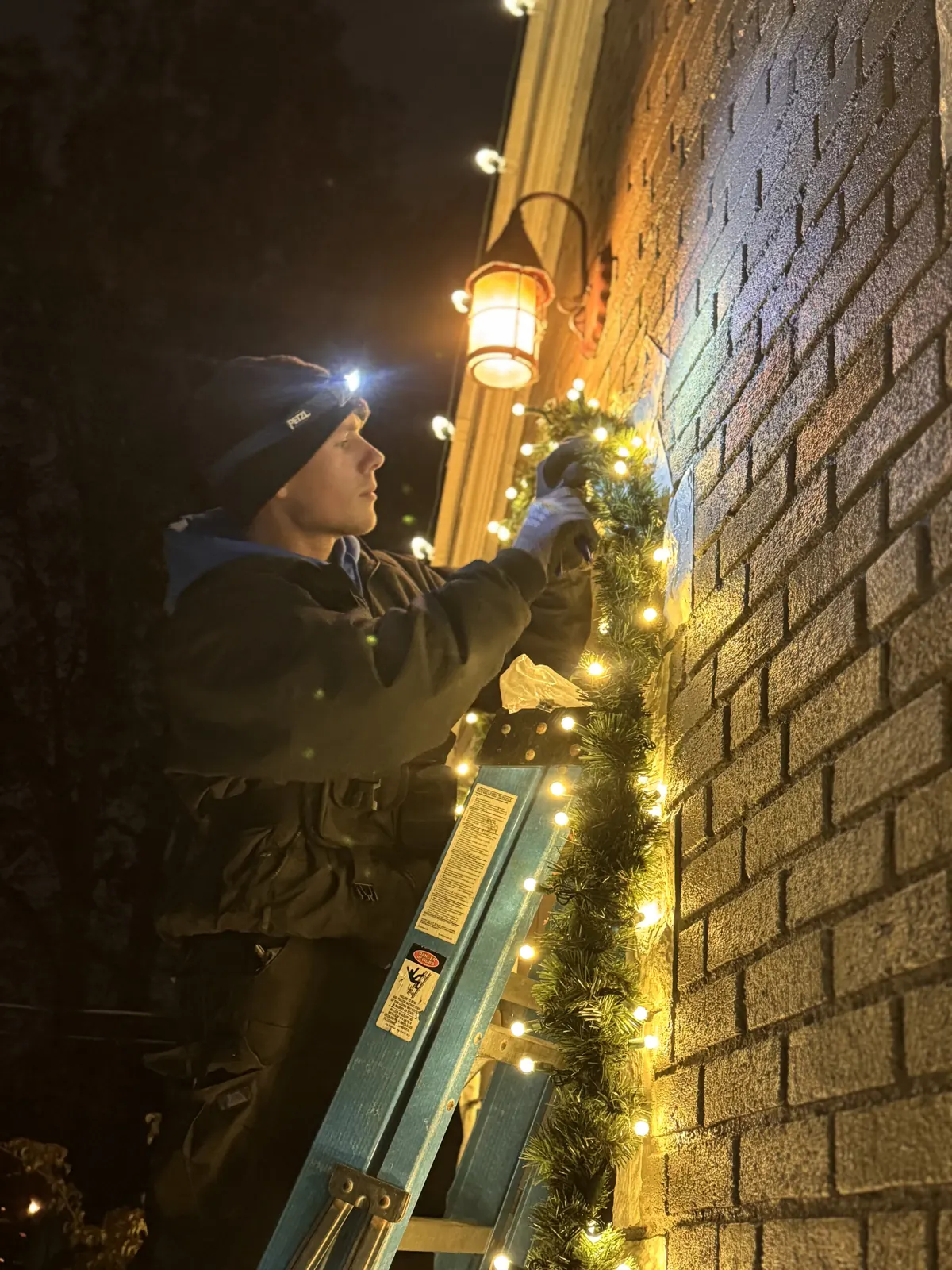 Frey Bros installer hanging lit Christmas garland on a brick entryway