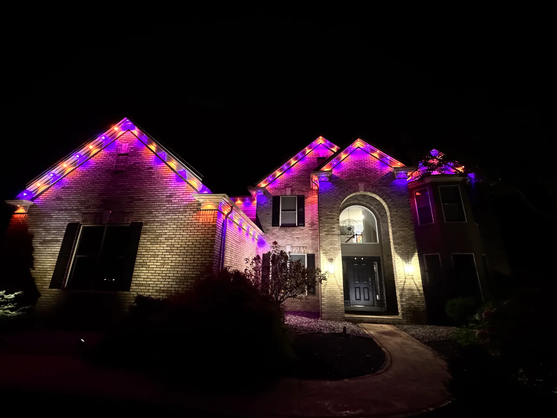 The same brick home at night with permanent lighting changed to purple, pink, and amber