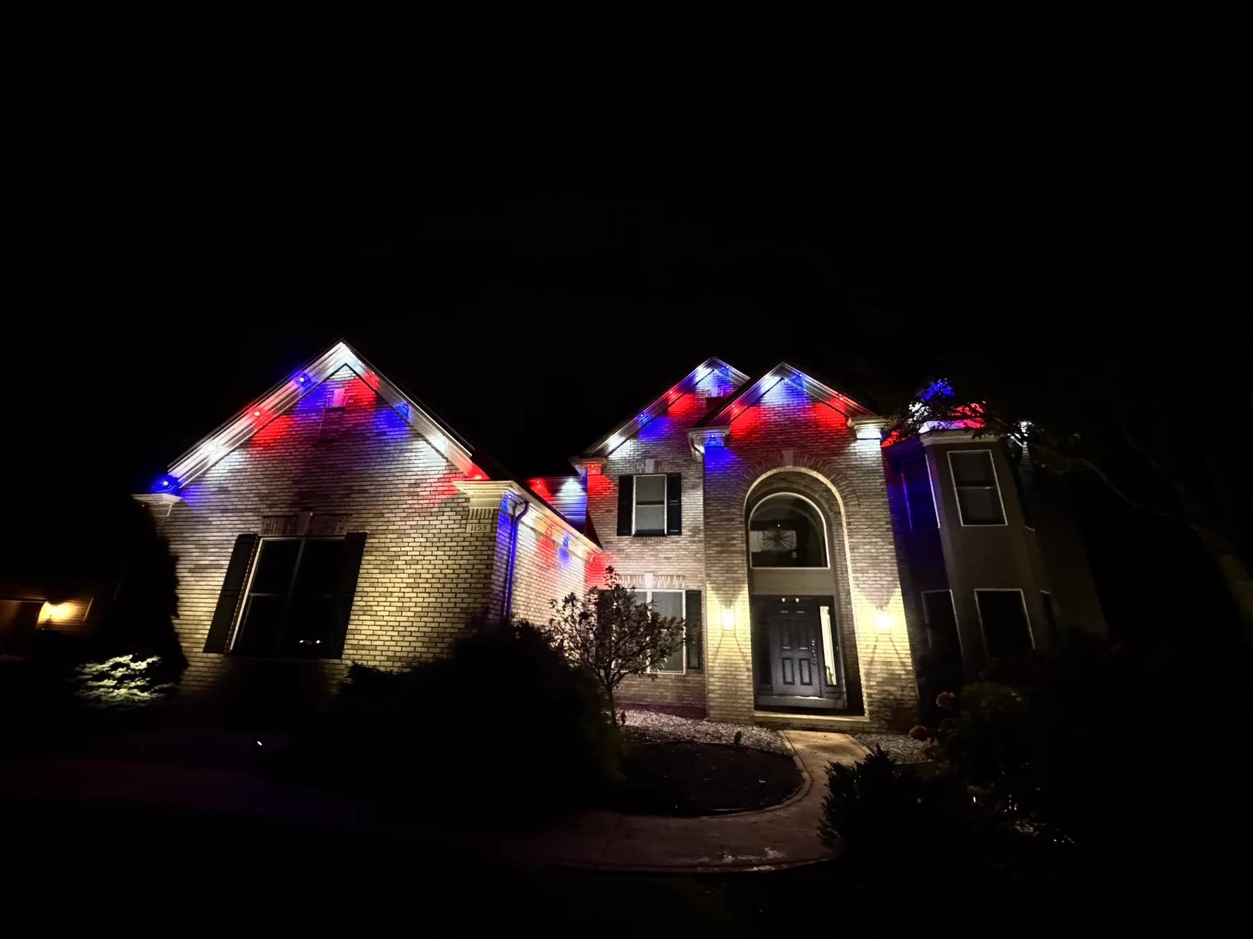 Permanent roofline lighting in red and blue across a brick home at night