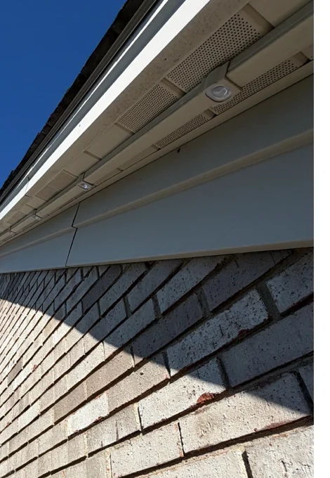 Daytime close-up of a permanent lighting track under a soffit, with the small lens sitting along the fascia