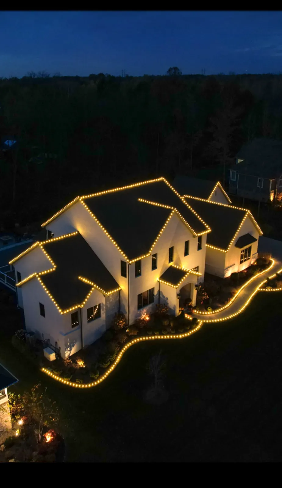 Aerial view of a home with mulch beds and walkways outlined in warm white Christmas border lighting