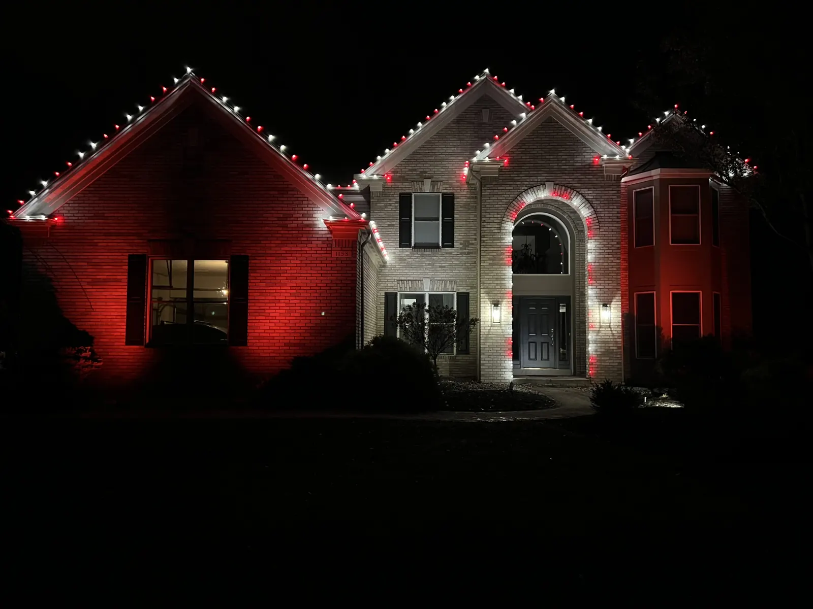 Red and white Christmas roofline lighting on a brick home